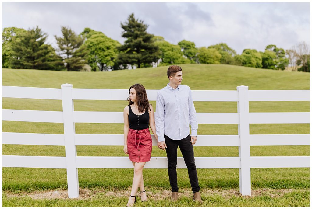 couple pose standing by fence looking opposite ways