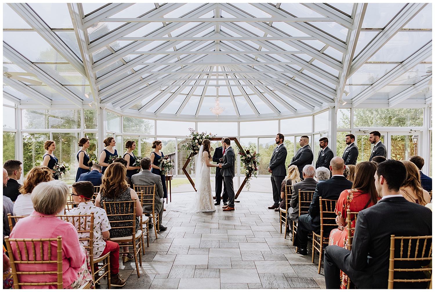 bride and groom holding hands during wedding ceremony in front of hexagon alter and in a green house