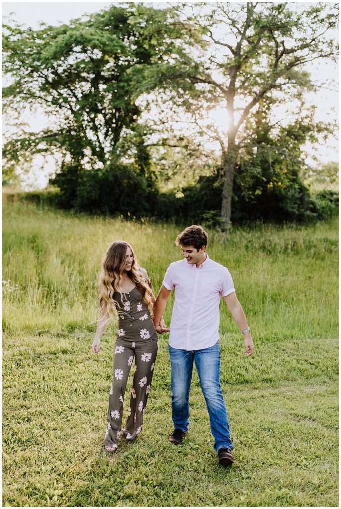couple walking and holding hands smiling in grass field