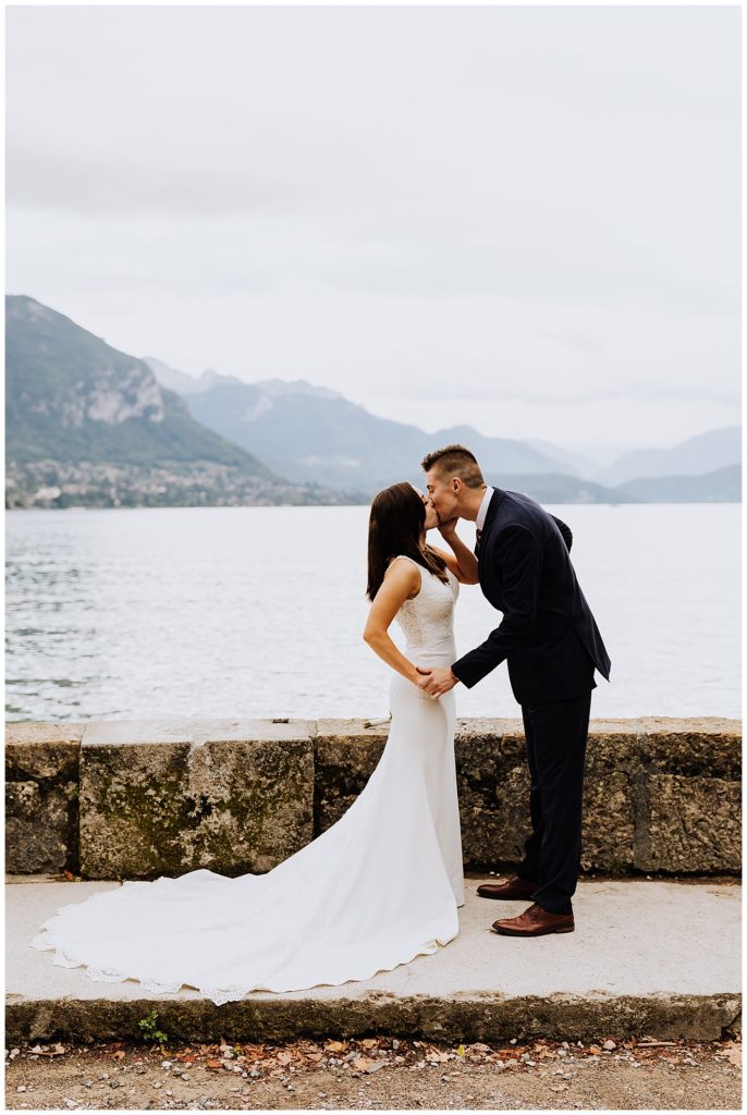 bride and groom kissing in front of mountains and lake annecy france