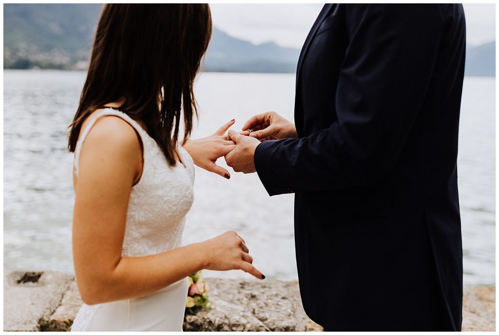bride and groom exchanging rings in front of mountains and lake in annecy france