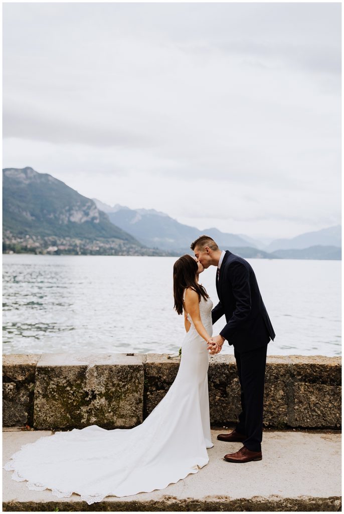 bride and groom kissing in front of mountains and lake in annecy france