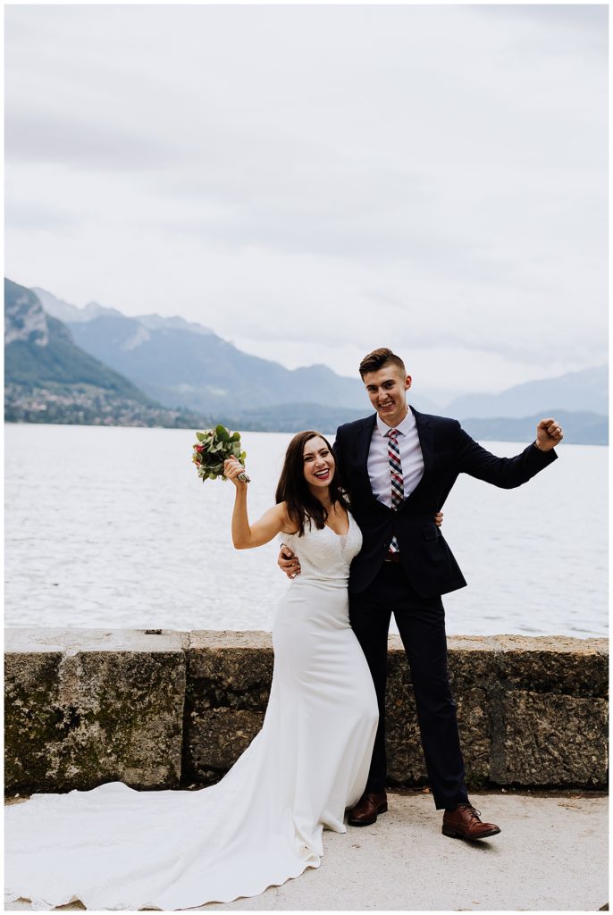 bride and groom celebrating marriage in front of mountains and lake in annecy france