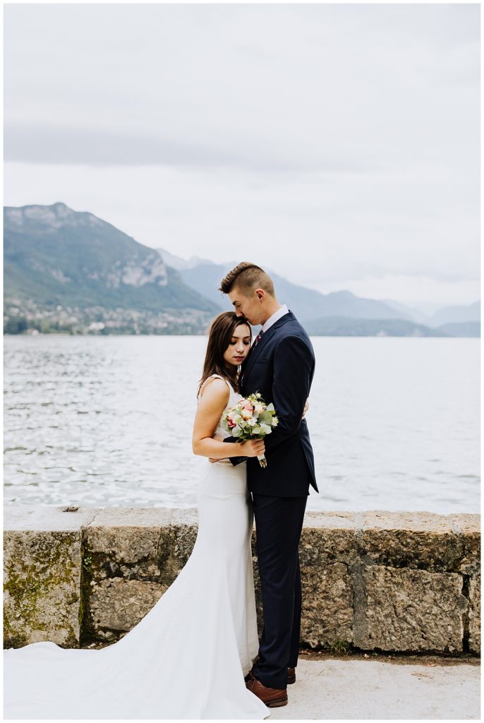 bride and groom hugging in front of mountains and lake in annecy france