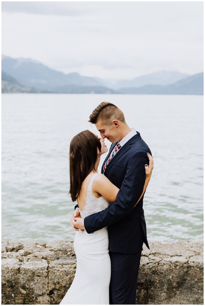 bride and groom hugging in front of mountains and lake in annecy france