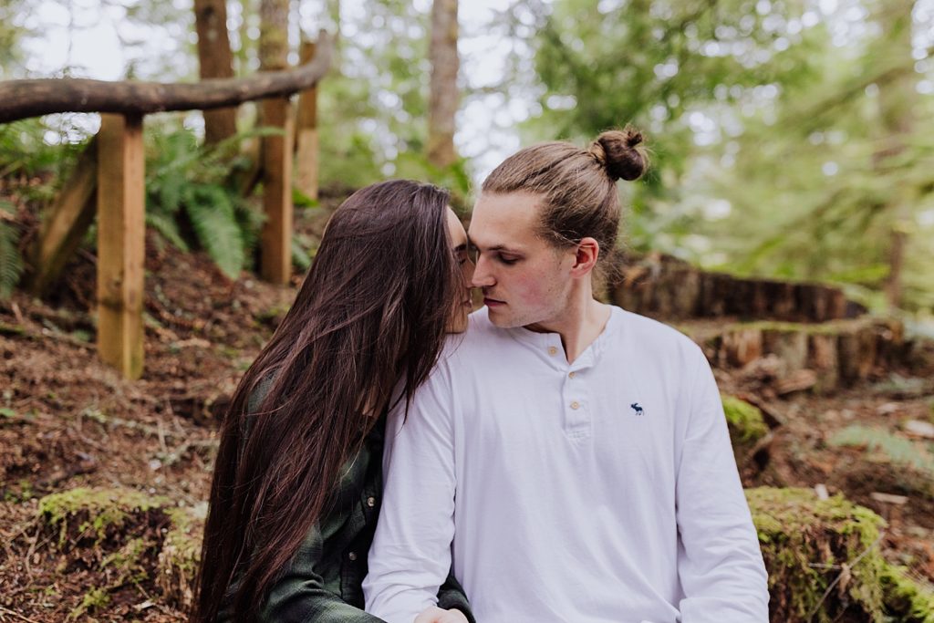 Oregon couple sitting in woods kissing