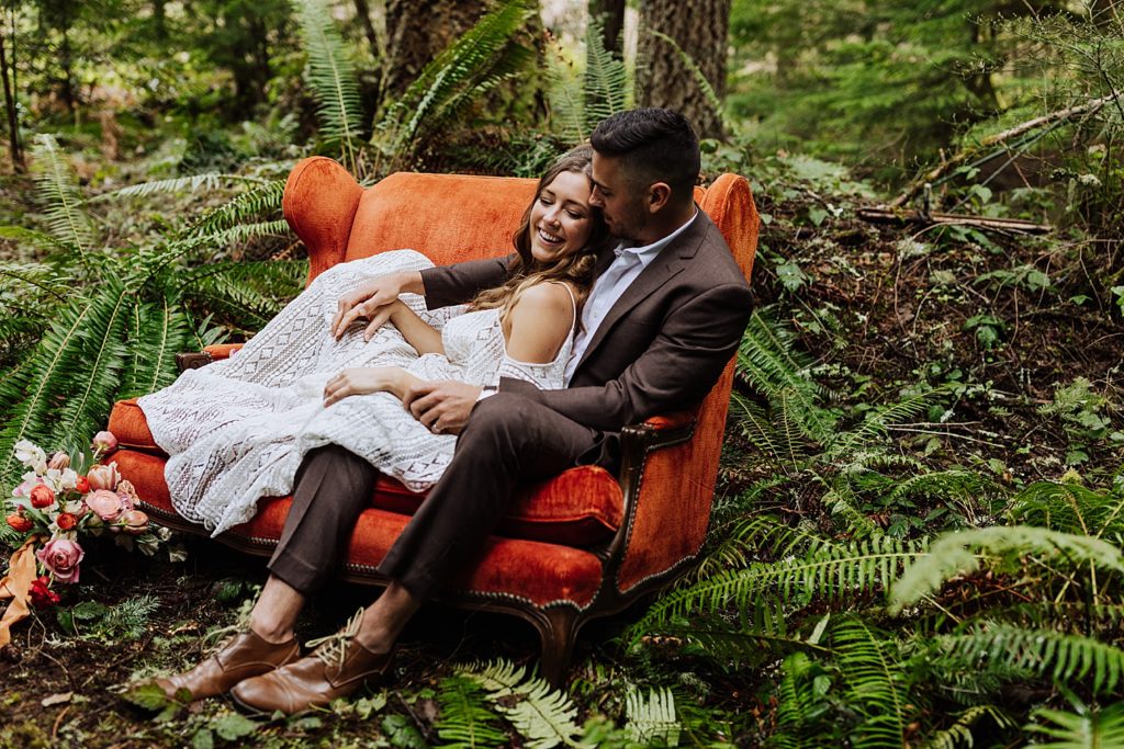 bride and groom sitting in orange couch in woods