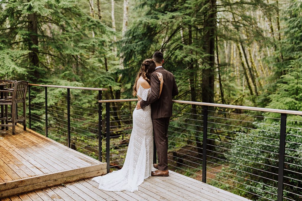 bride and groom standing on deck in middle of woods first look