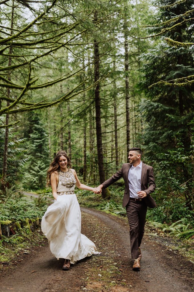 bride and groom running together on path in woods
