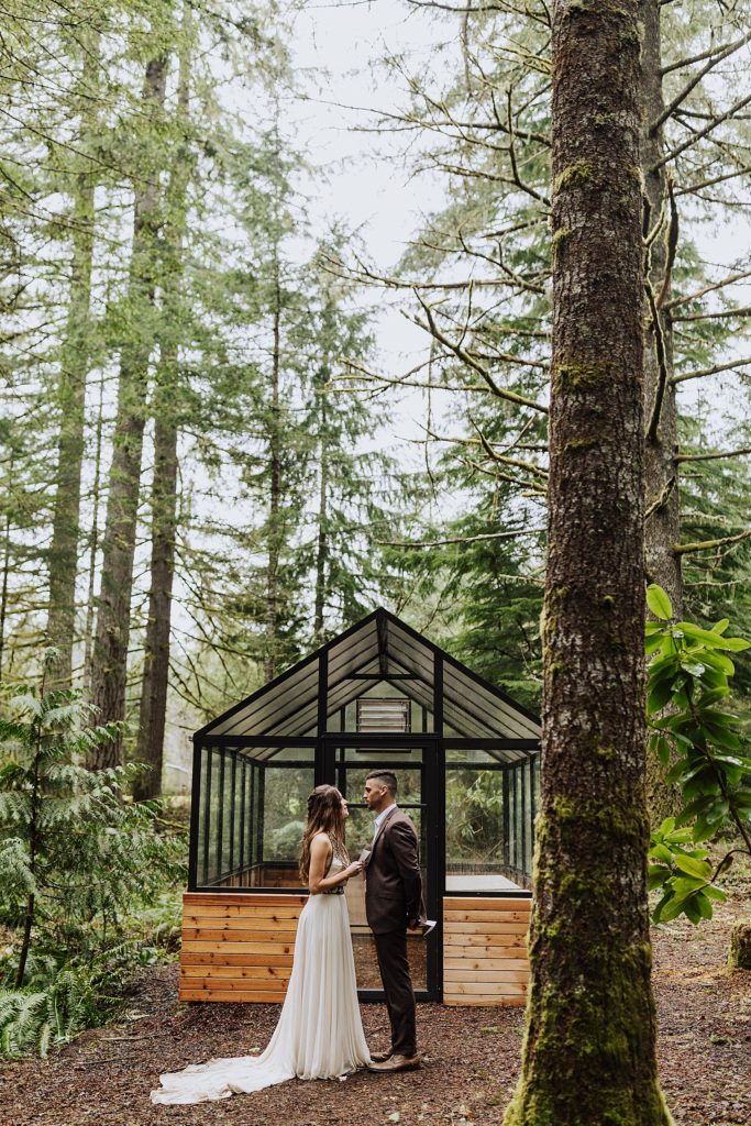 bride and groom eloping in front of greenhouse in woods