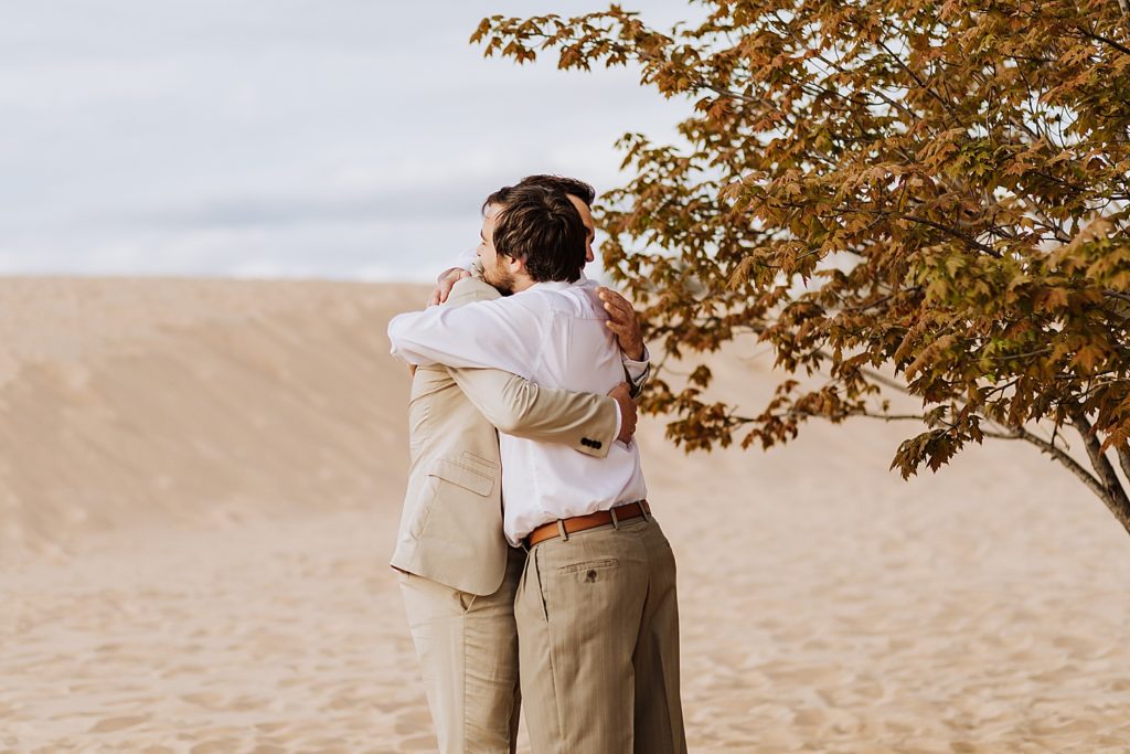 officiant and groom hugging before ceremony on beach