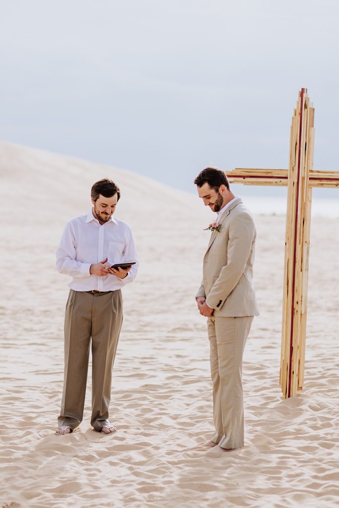 officiant and groom right before bride walks down aisle on beach