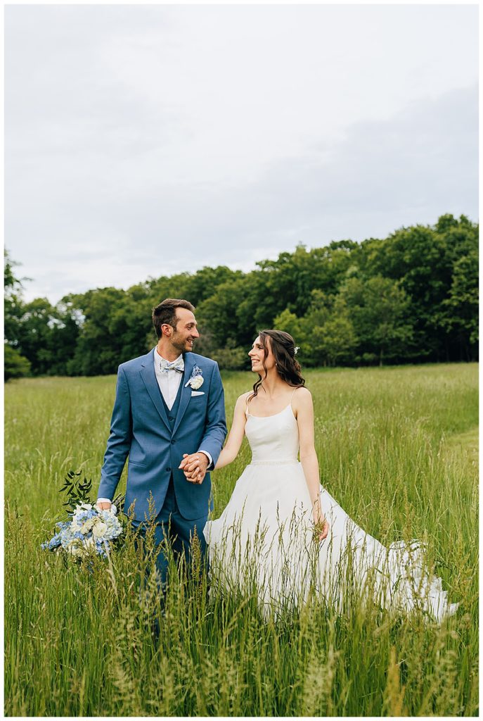 Wife smiles at husband in green field by Kayla Bouren Photography
