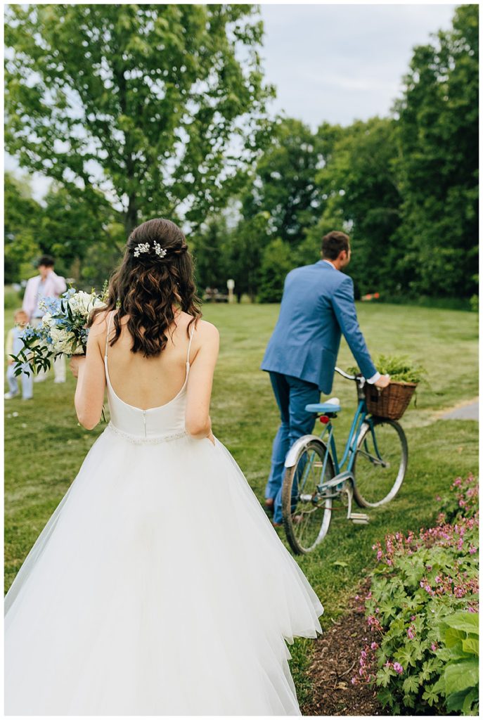 Wife watches husband move vintage bike at Cushing Field House wedding