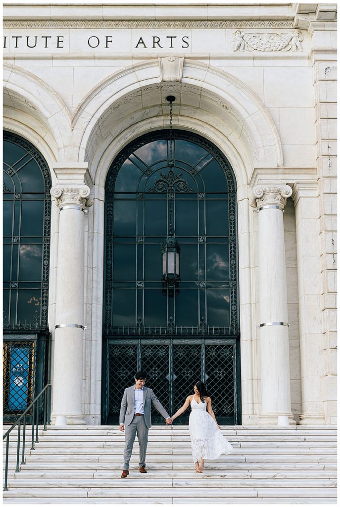 Couple holds hands on stairs during Detroit Institute of the Arts Engagement Session