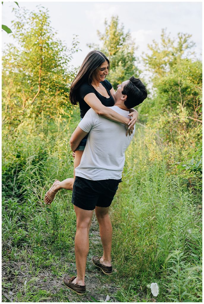 Man picks up woman in green field for Detroit Wedding Photographer
