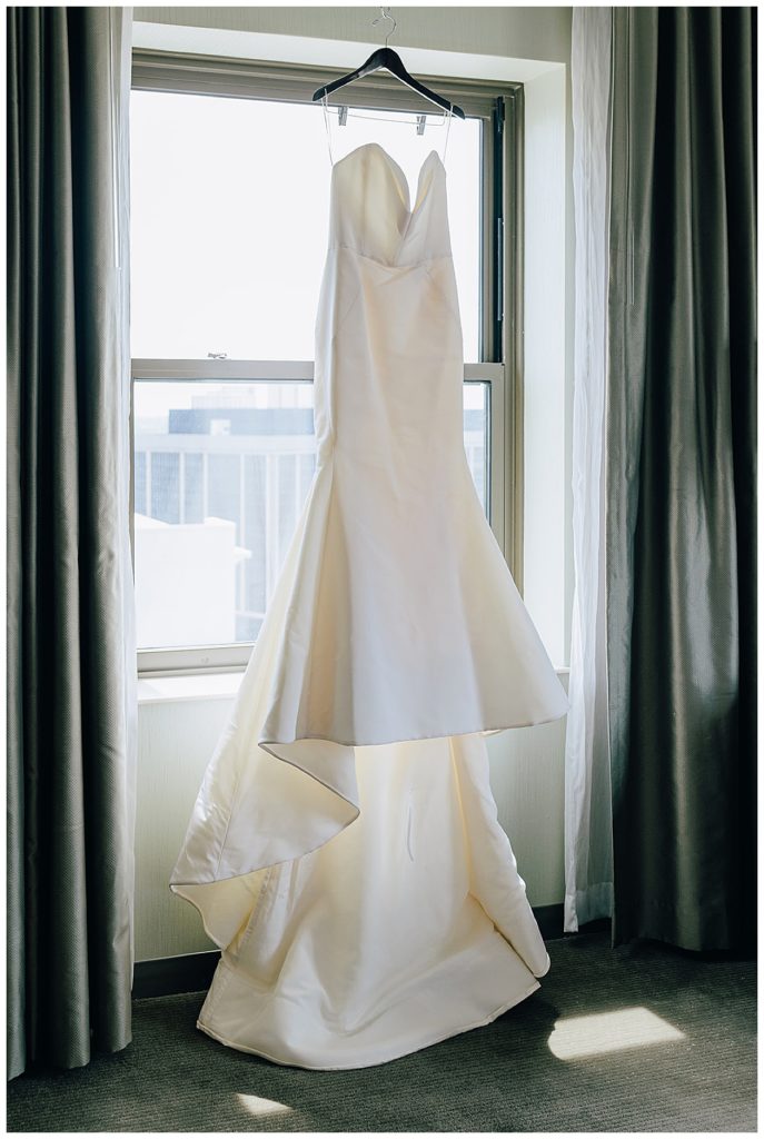 Bridal gown hangs fro window sill by Detroit Wedding Photographer.