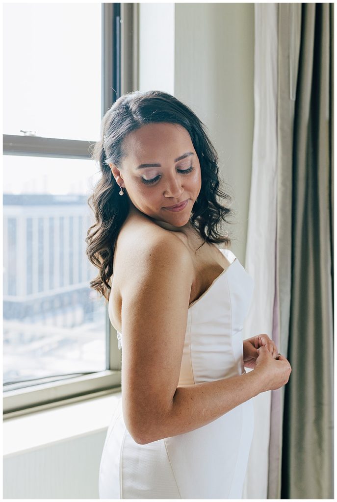 After getting ready bride is looking down at shoulder in wedding dress by Kayla Bouren photography.