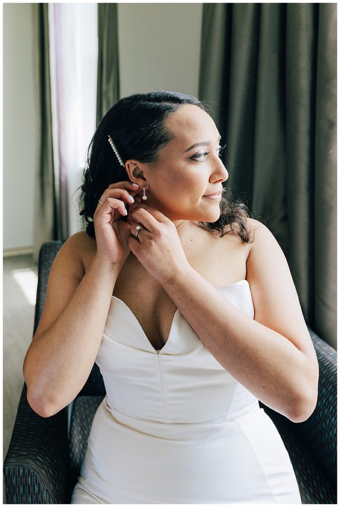Bride adjust jewelry while looking out window by Detroit Wedding Photographer.
