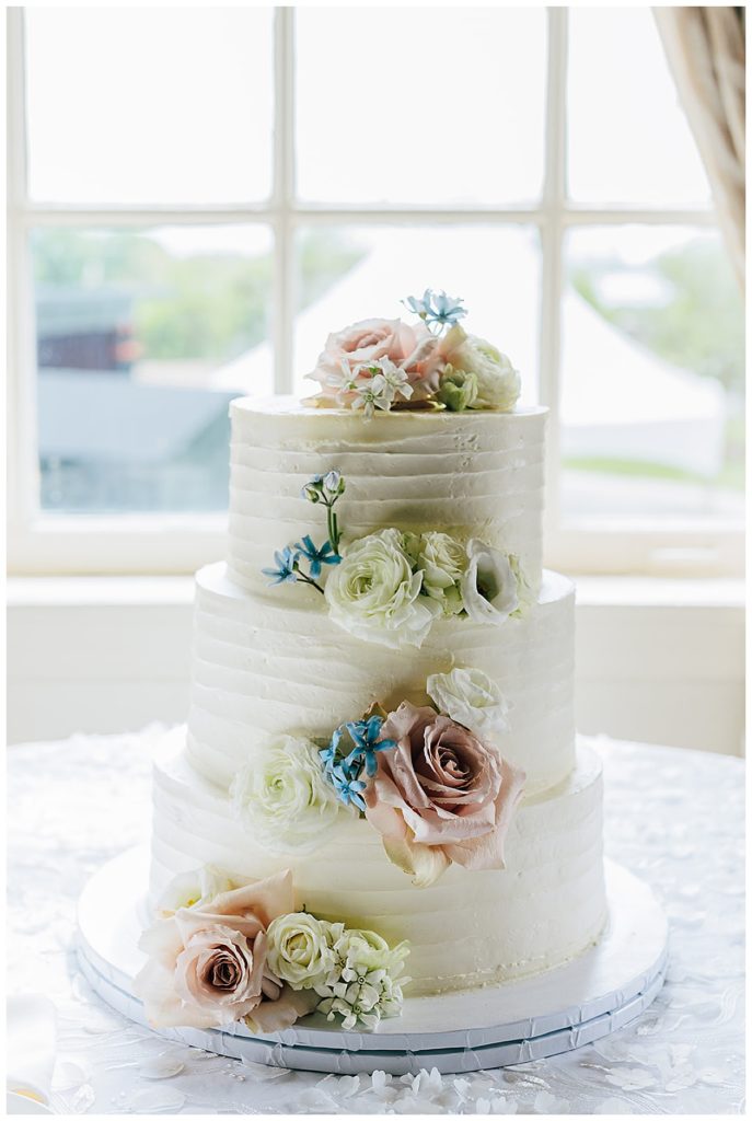 The white wedding cake is covered in beautiful pink and white roses with a small blue touch by Kayla Bouren photography.
