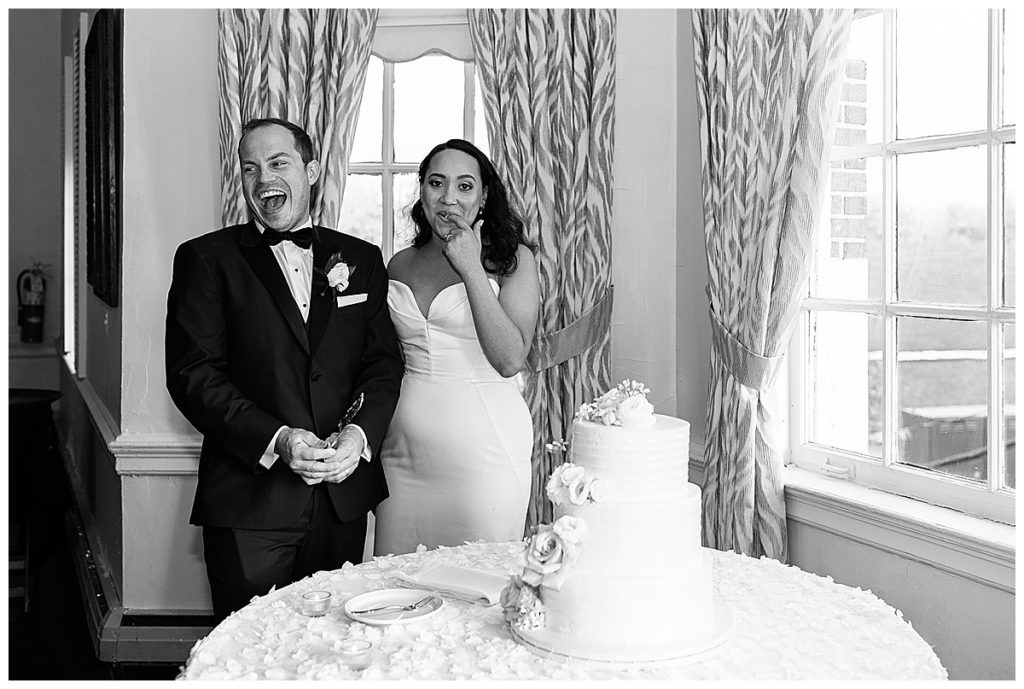 Couple shares laughs and smiles in front of cake for elegant Yacht Club wedding.