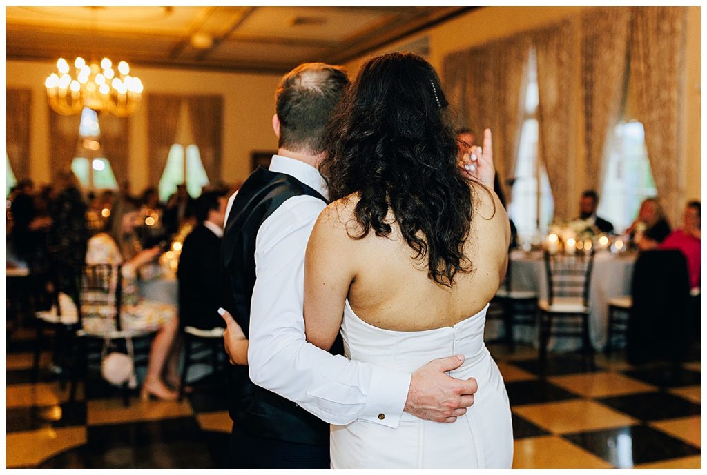 Couple share a hug while looking at friends and family by Detroit Wedding Photographer.