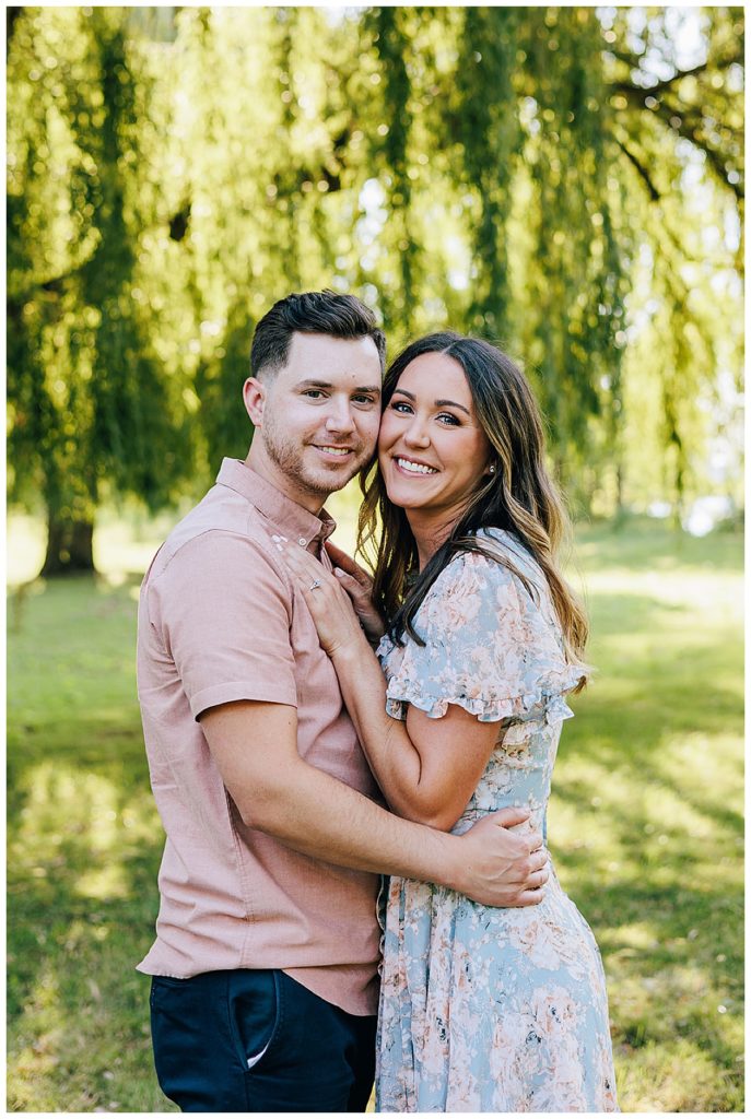 Engaged couple smile under willow tree for Kayla Bouren Photography