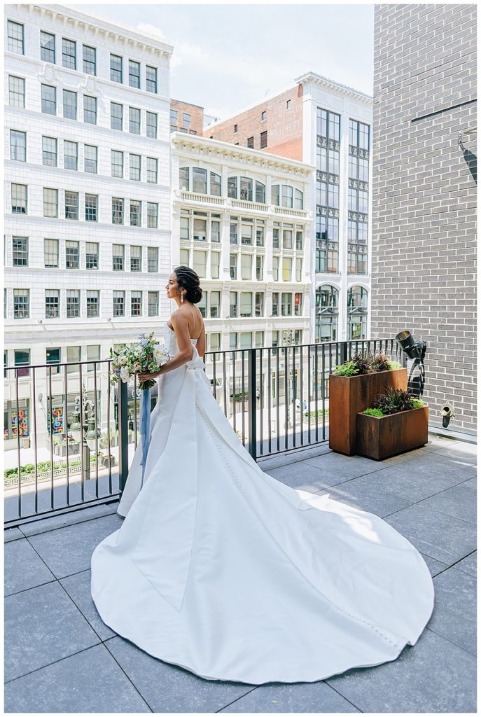 Bride stands against balcony rail by Michigan Wedding Photographer