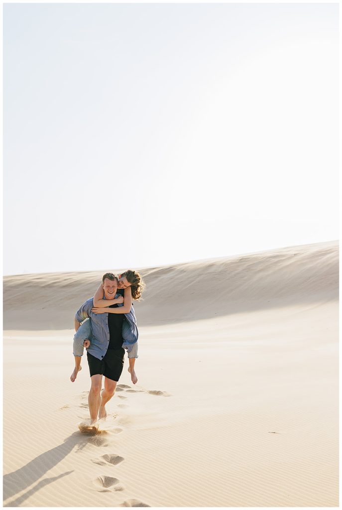 Woman on mans back during Silver Lakes Sand Dunes Engagement Session.