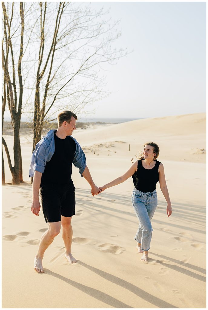 Man and woman walking hand in hand in sand for Kayla Bouren Photography.