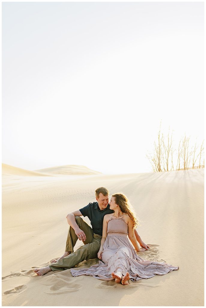 Woman and man sit in sand for Silver Lakes Sand Dunes Engagement Session.