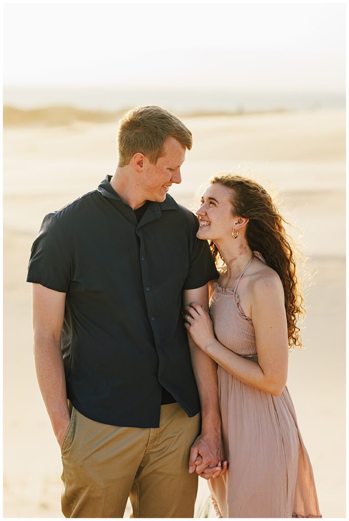 Woman holds onto man during Silver Lakes Sand Dunes Engagement Session.
