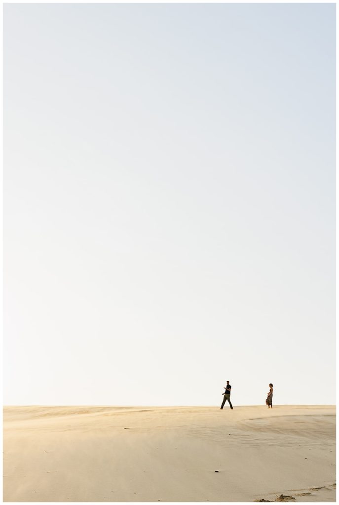 Couple walks across sand during Silver Lakes Sand Dunes Engagement Session.