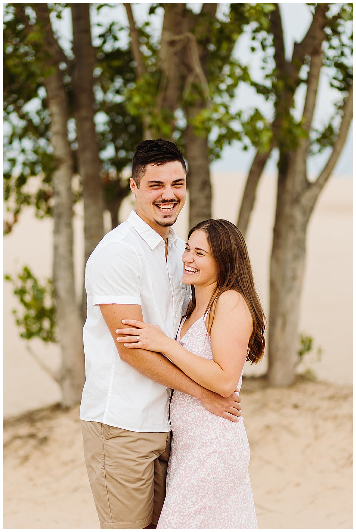 Fiancés laugh by a tree in the san dunes for Detroit Wedding Photographer