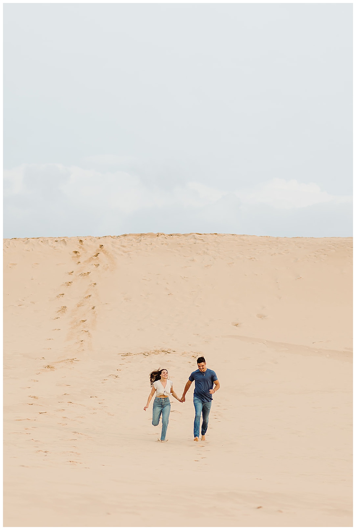 Two people run down the sand dune for Mears, MI Engagement session