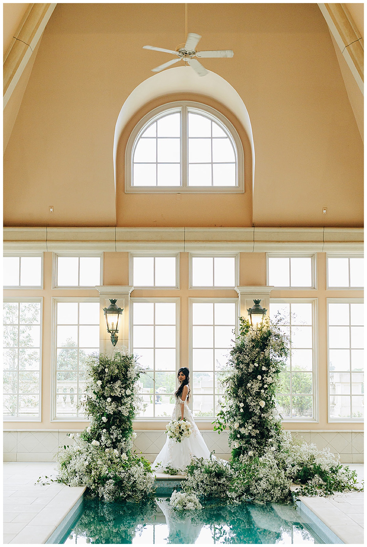 Woman stands under arch floral install and pool for Kayla Bouren Photography