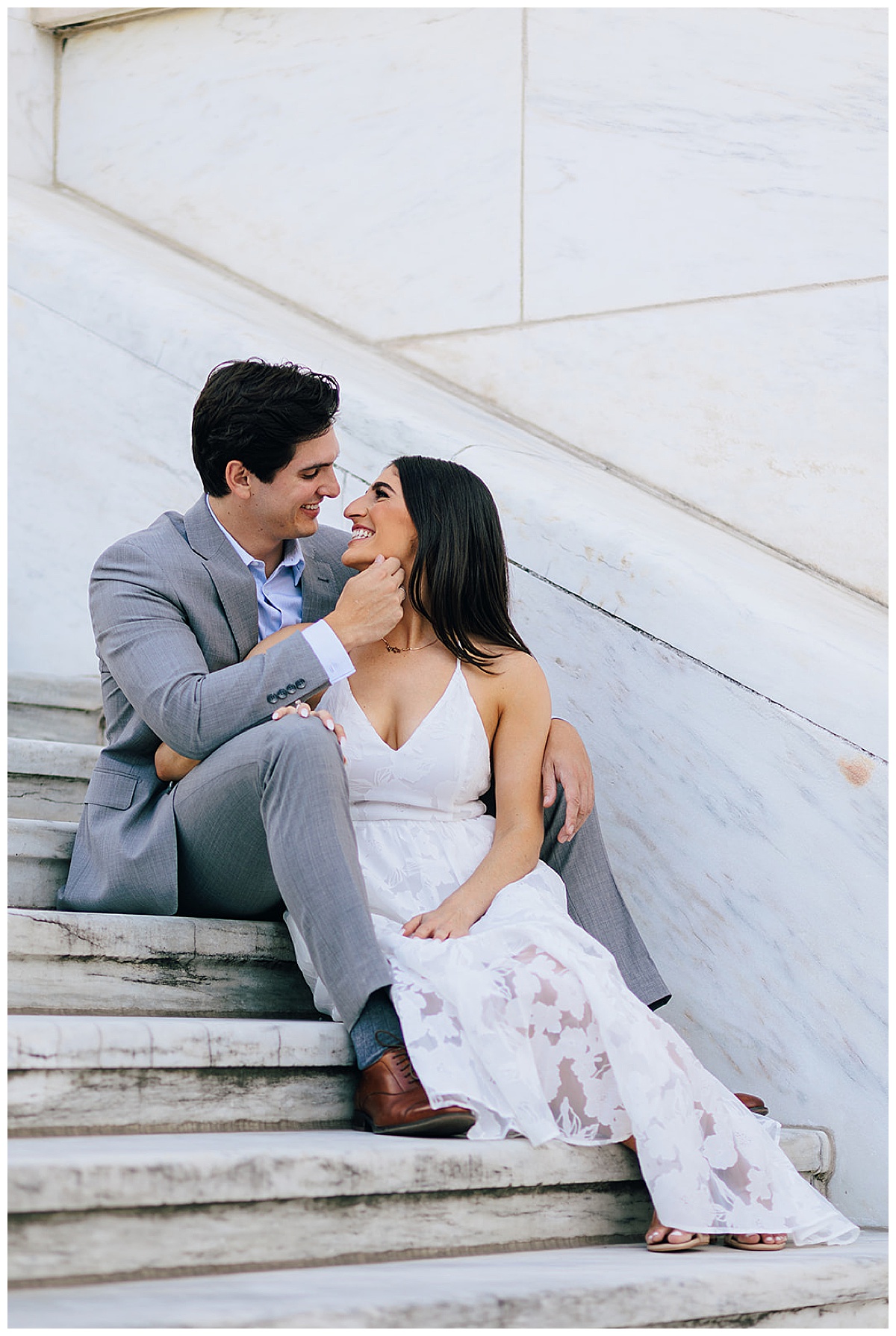 Man pulls woman face toward him as they share smiles together while sitting on the steps at one of the Iconic Detroit Locations for Your Engagement Session