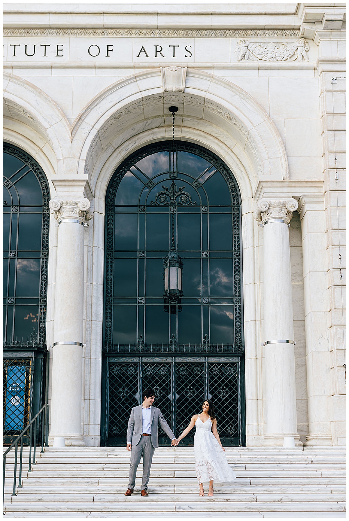 Man and woman hold hands together and sit on steps at at one of the Iconic Detroit Locations for Your Engagement Session